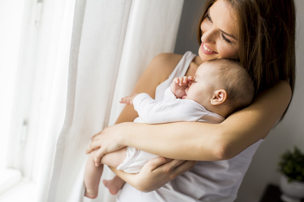Happy mother with newborn baby girl by window